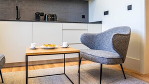 Een moderne keuken met een grijze betegelde spatwand, een koffiezetapparaat, een broodrooster en een eettafel met een stoel.