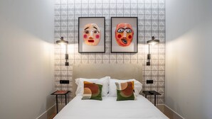 Ein Hotelzimmer mit einem Bett, zwei gerahmten Kunstwerken an der Wand und zwei Nachttischen mit Lampen.