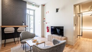 Un salon moderne avec un plancher en bois, des fauteuils à revêtement gris, une table basse et un téléviseur à écran plat.