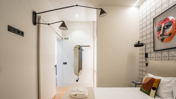 Une chambre d’hôtel moderne équipée d’un lit, d’une table de chevet, d’un miroir fixé au mur et d’un porte-serviettes.