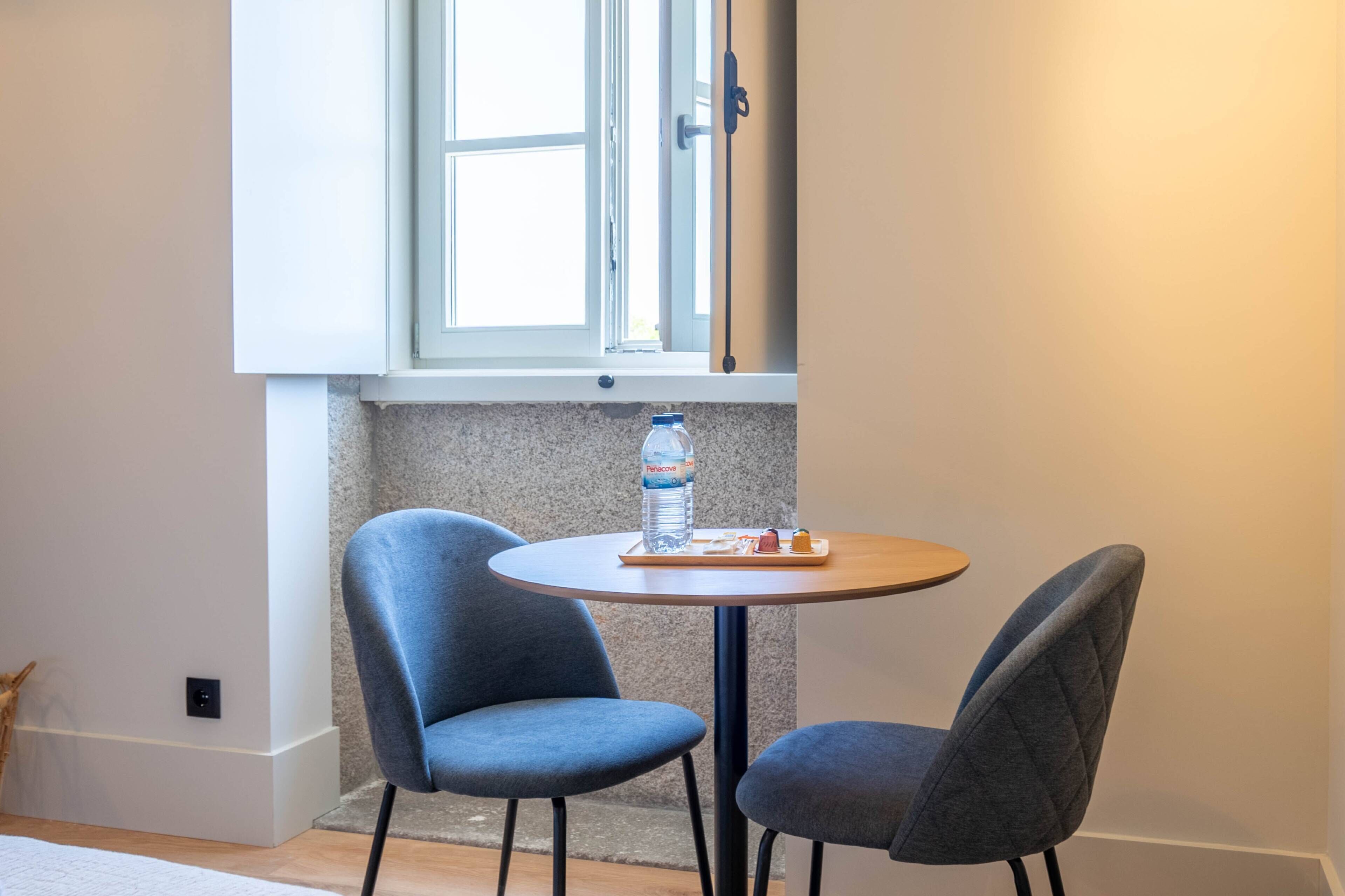 Una habitación pequeña con una mesa redonda y dos sillas, una ventana y una botella de agua sobre la mesa.