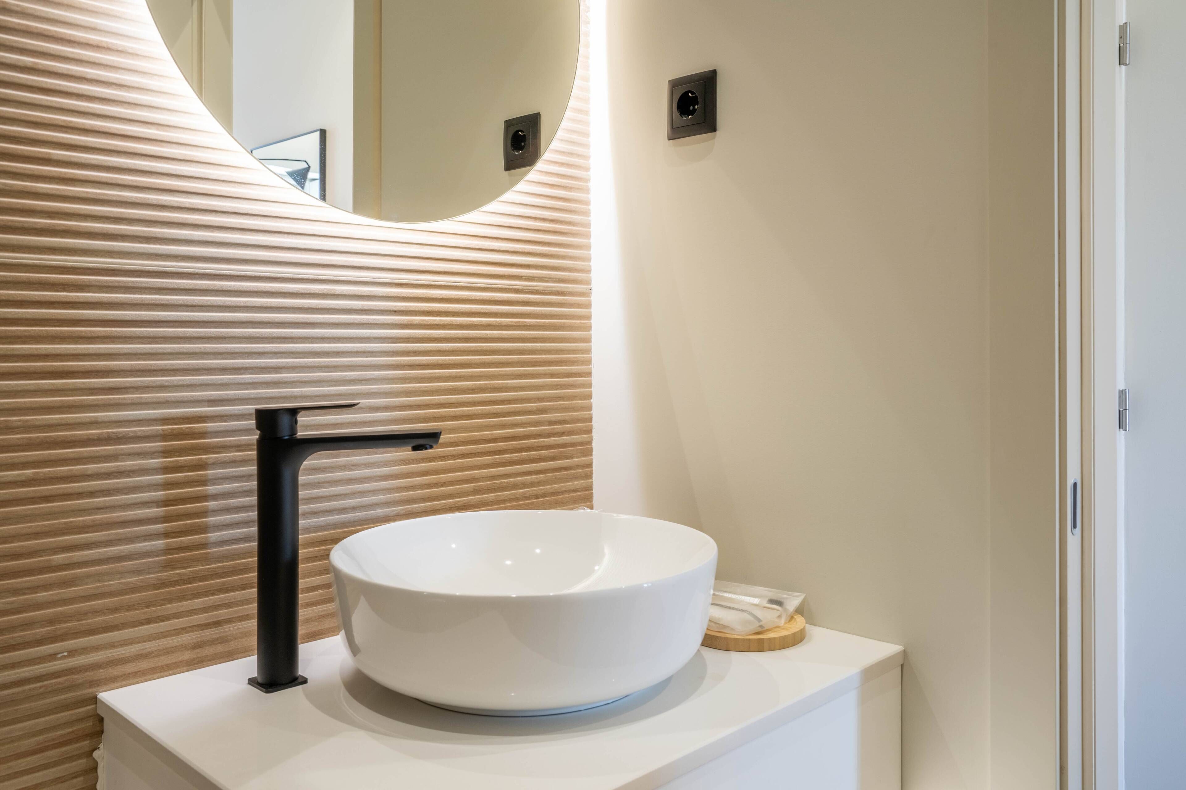 A modern bathroom with a white sink, black faucet, and a wooden slatted wall.