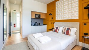 Habitación de hotel con una cama grande, una kitchenette y un baño visible a través de una puerta abierta.