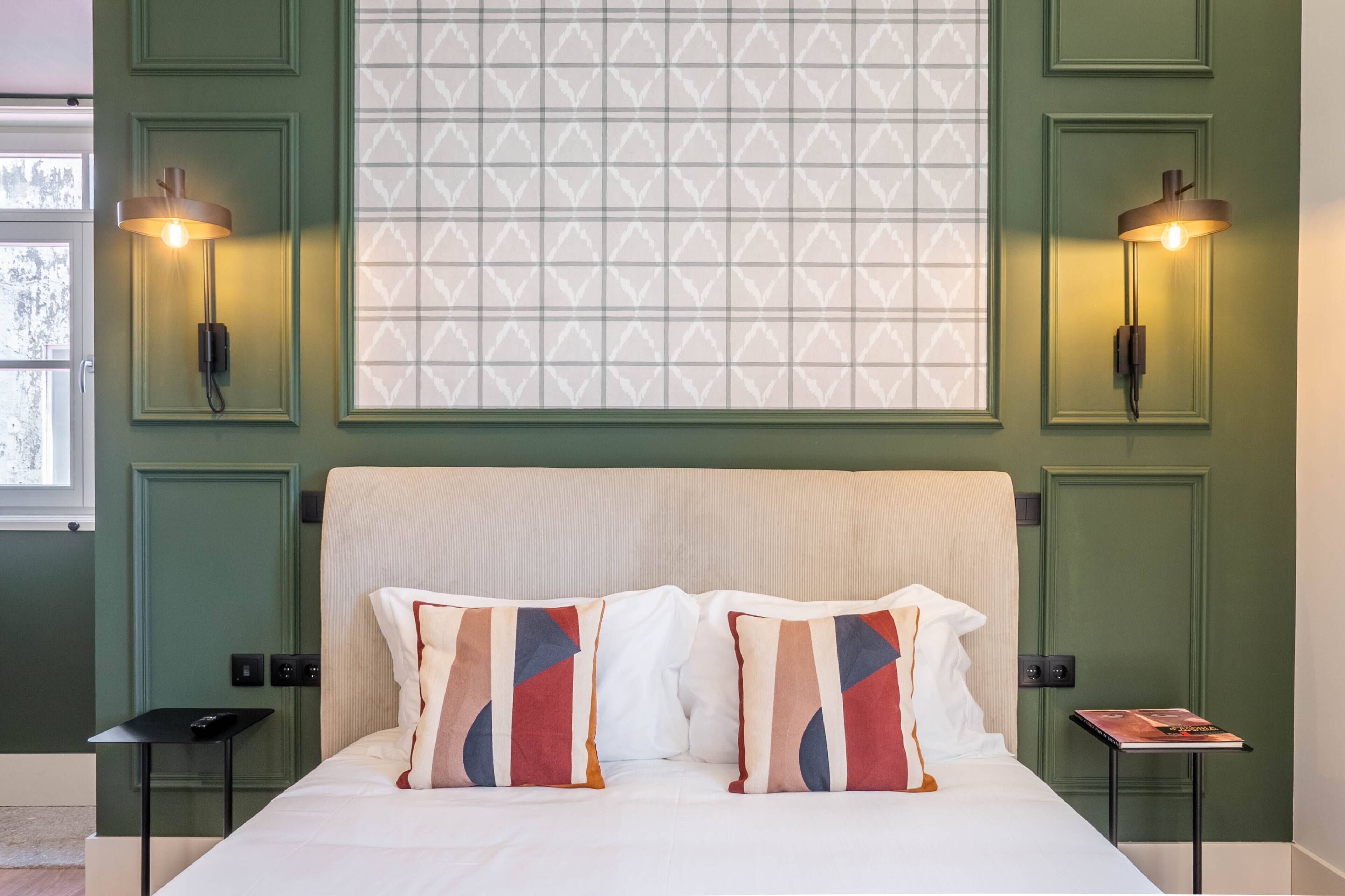 A neatly made bed with two pillows, a bedside table with a book, and two wall-mounted lamps.