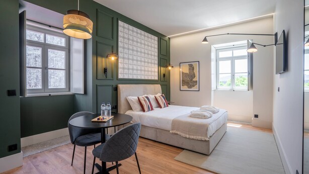 Een moderne slaapkamer met een bed, bureau en stoel. Er is een raam met uitzicht op het landschap.