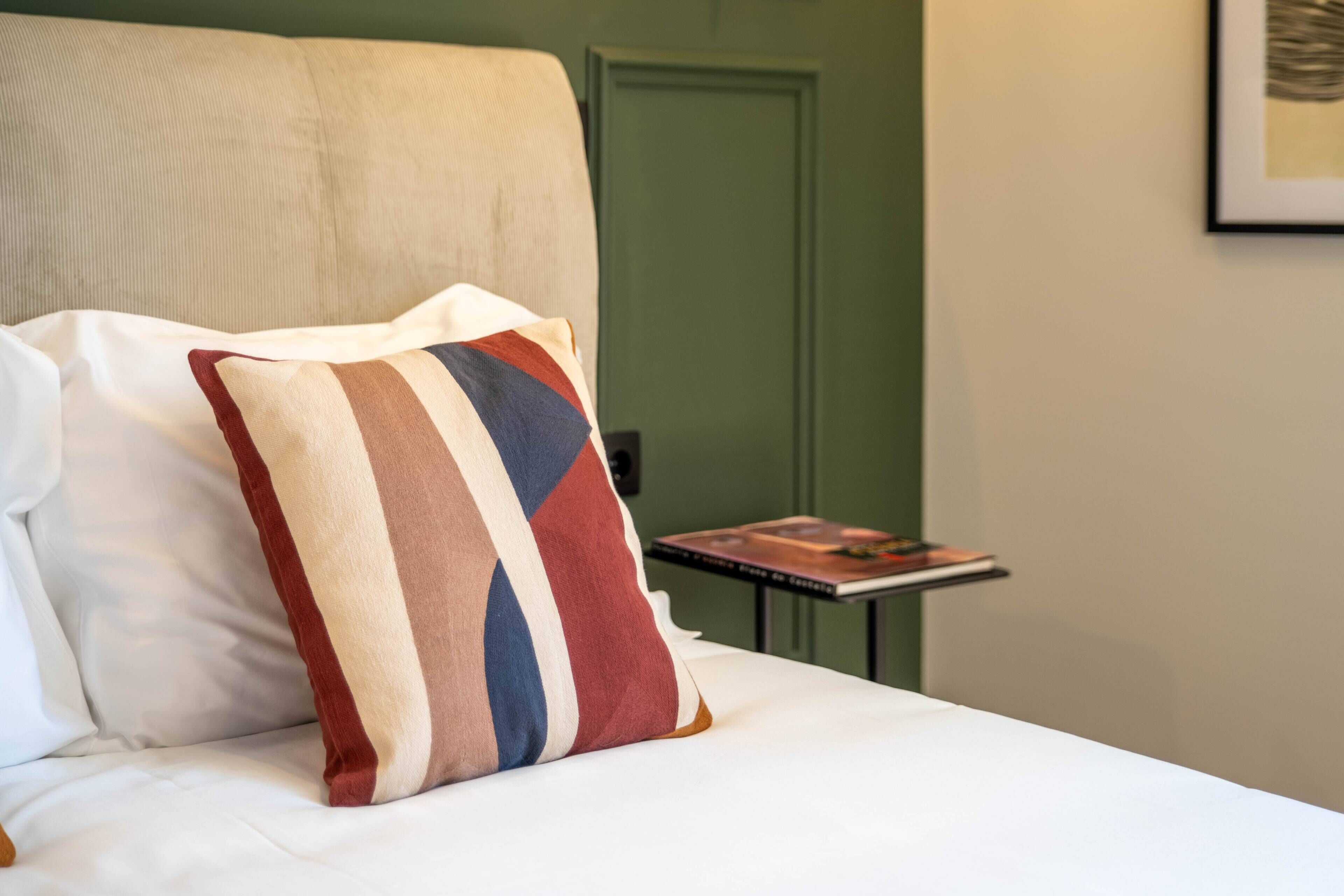 A neatly made bed with a striped pillow and a small table with a book beside it.