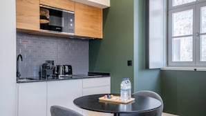 Een moderne keuken met witte kasten, een backsplash in een visgraatmotief en een zwart aanrecht. Op de tafel staat een waterfles, en er is een raam met uitzicht op bomen.