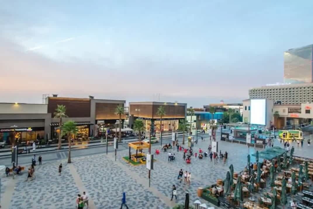 Ett stort och rymligt offentligt torg med moderna byggnader, utomhusmöbler och palmer.