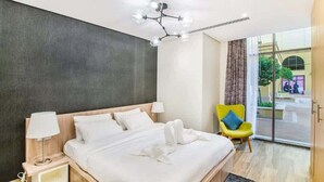 Une chambre d’hôtel moderne avec un grand lit, une table de chevet avec une lampe, une chaise jaune vif et une vue sur l’extérieur grâce à une porte vitrée.