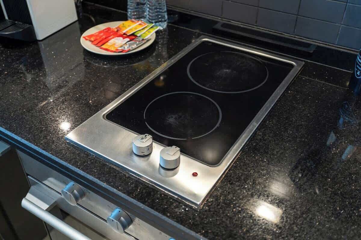 A kitchen with a black granite countertop, a stainless steel induction cooktop, and a built-in oven below.