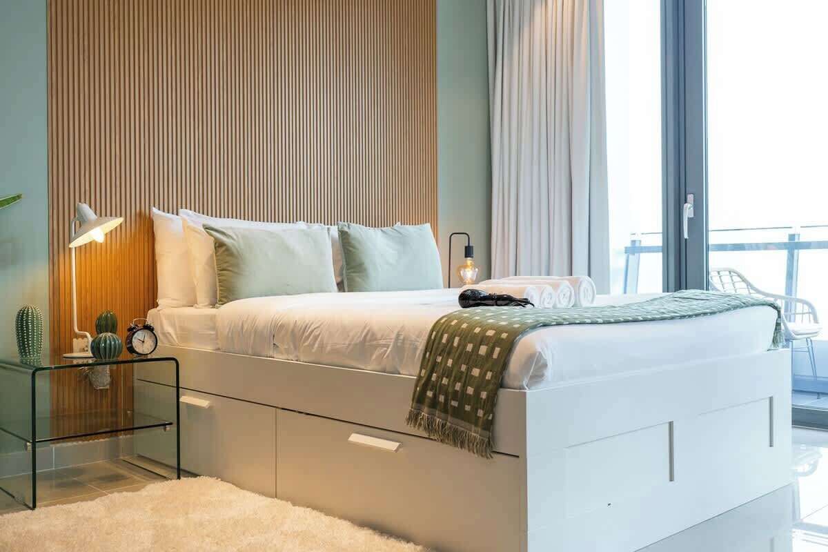 Ein modernes Schlafzimmer mit Bett, Nachttischen, einer Lampe und Blick ins Freie.