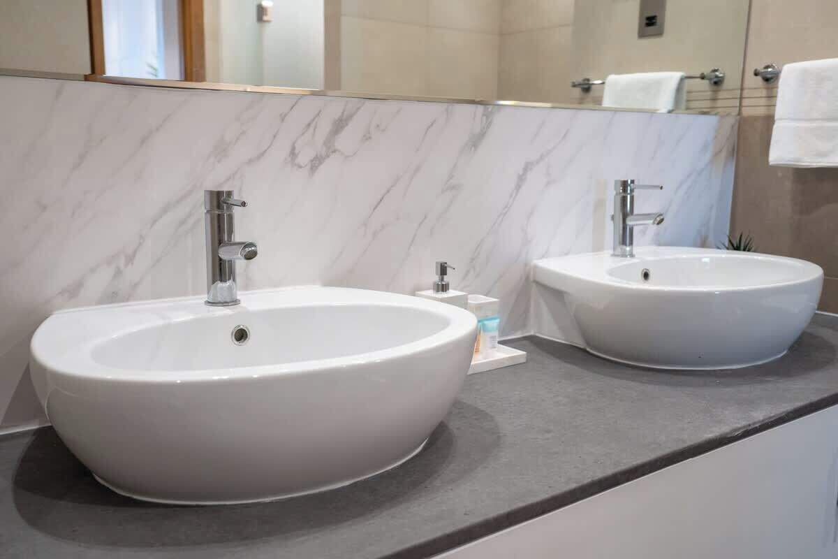 Une salle de bain avec deux lavabos ovales blancs, un miroir et un porte-serviettes.
