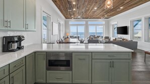 Un'ampia cucina con un'isola grande, soffitto in legno e vista sull'oceano.