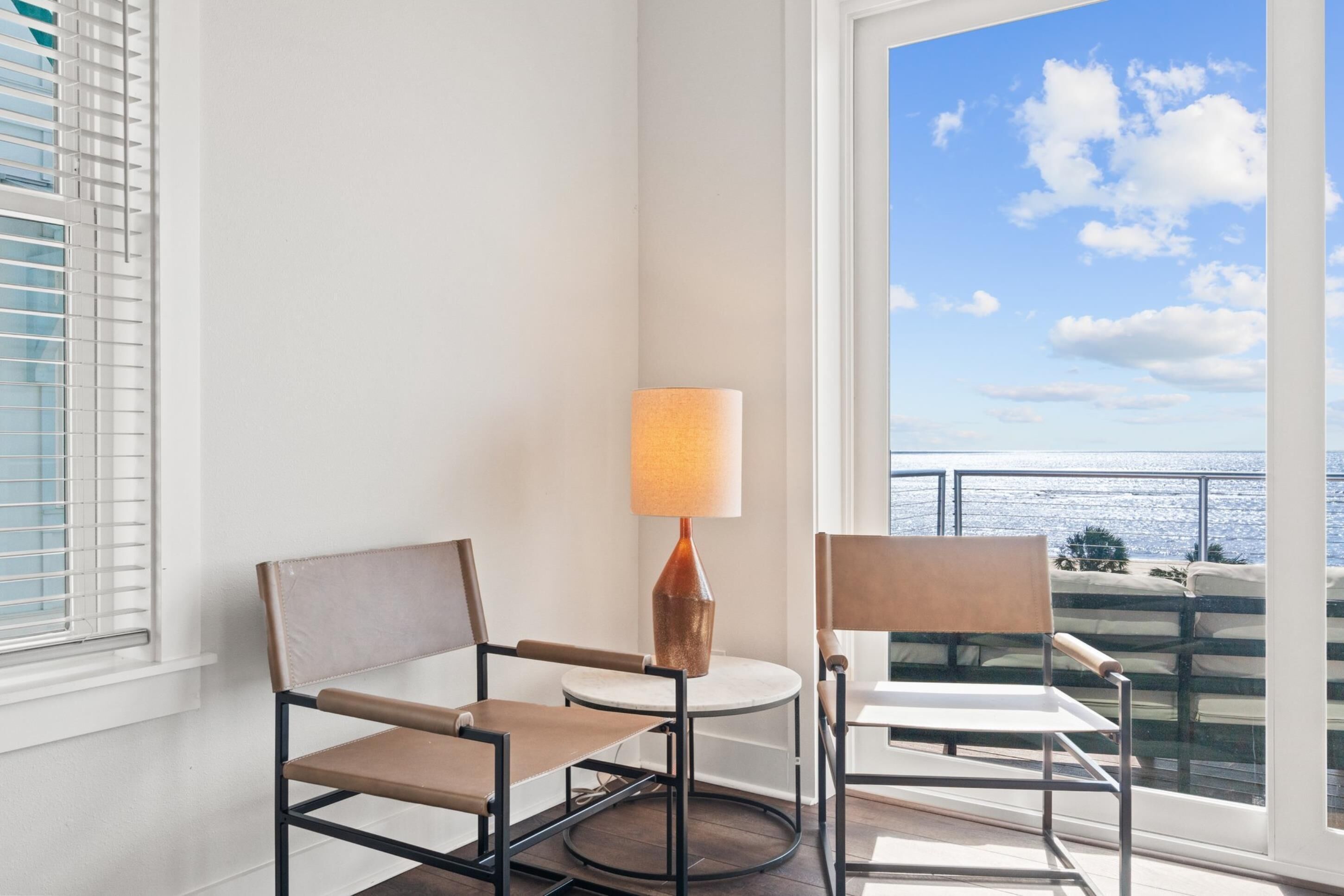 A balcony with two chairs and a table, a lamp, and a view of the ocean.