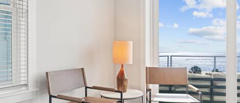 A balcony with two chairs and a table, a lamp, and a view of the ocean.