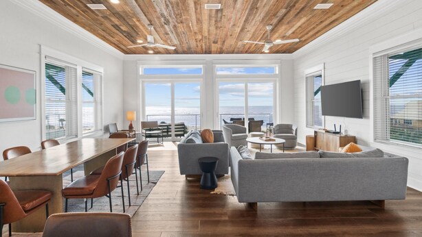 Un'ampia zona giorno con soffitto in legno, ampie finestre e vista sull'oceano.