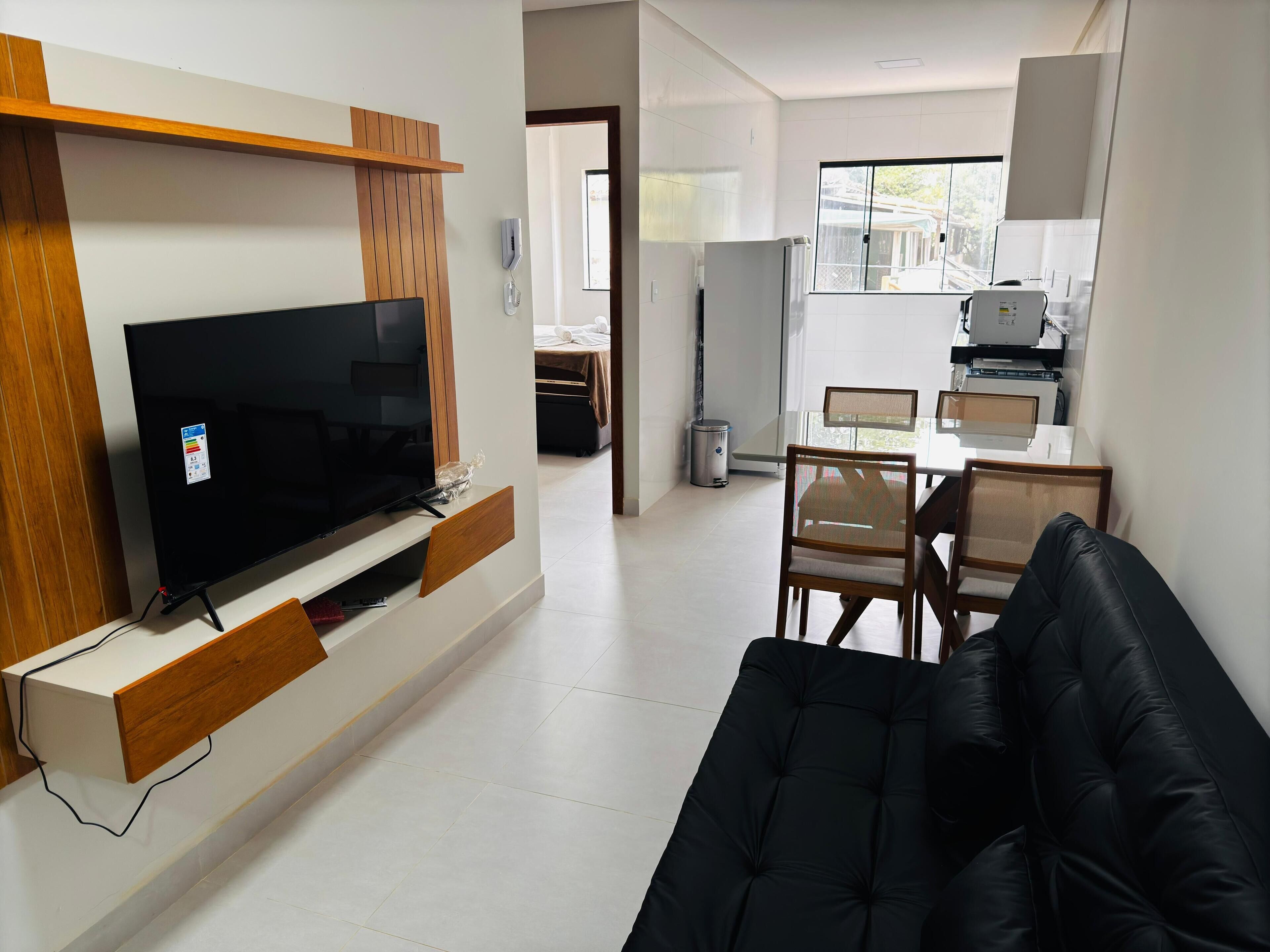 Una sala de estar moderna con una televisión de pantalla plana, un sofá negro y una zona de comedor con una mesa y sillas.