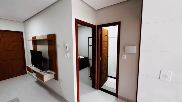Une chambre d’hôtel moderne dotée d’un téléviseur à écran plat fixé au mur, d’une porte en bois et d’une salle de bain visible à travers une porte ouverte.
