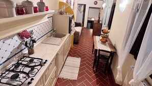 Une cuisine étroite équipée d’une cuisinière à gaz, de placards et d’un coin repas avec une table et des chaises.
