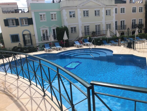 A swimming pool with a metal railing, surrounded by lounge chairs and umbrellas.