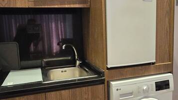 A compact kitchen with a microwave, refrigerator, sink, and washing machine.