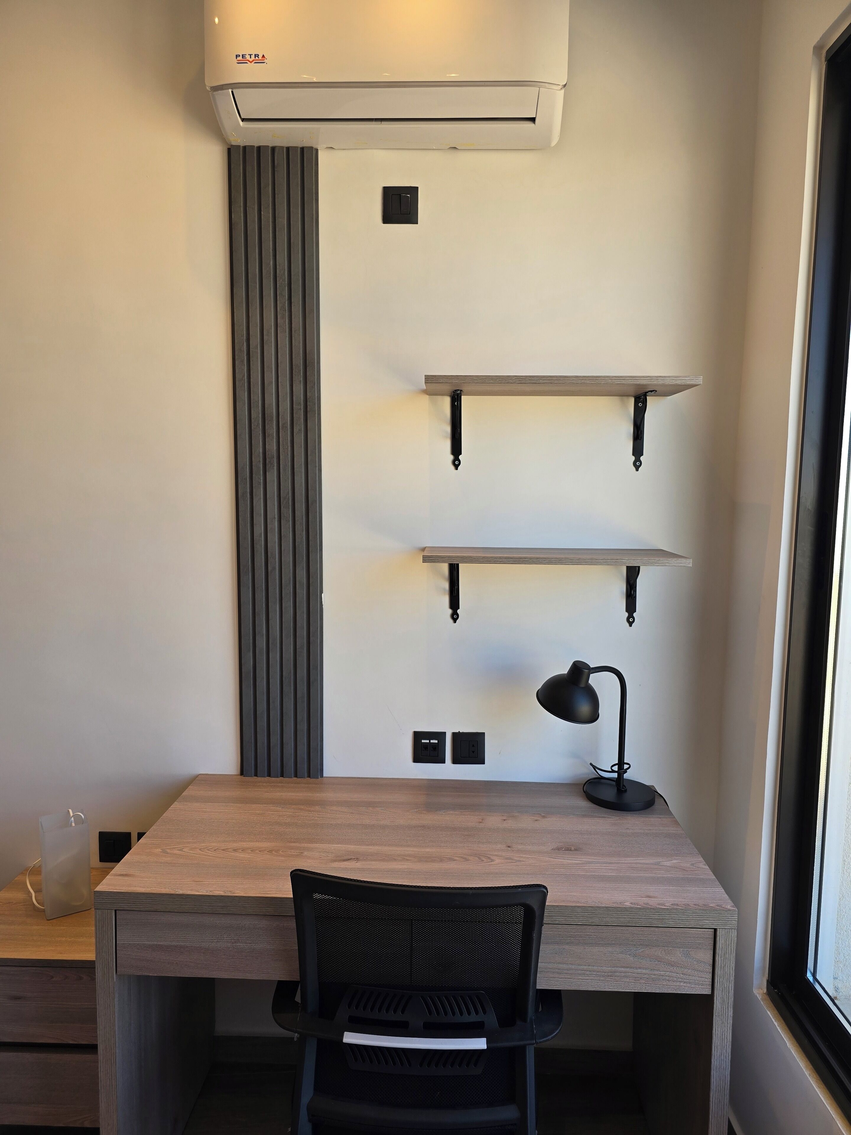 A modern office space with a wooden desk, black mesh chair, and a wall-mounted air conditioner.