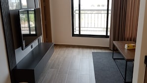 Ein modernes Hotelzimmer mit großem Fenster, einem Flachbildfernseher, einer hölzernen Sitzbank und einem kleinen Tisch.