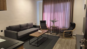 Ein modernes Wohnzimmer mit grauem Sofa, zwei Sesseln, einem kleinen Tisch und einem Fernseher.
