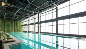 An indoor swimming pool with clear glass walls, a tiled floor, and a ceiling with exposed ductwork.