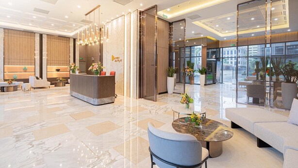 A modern hotel lobby with a reception desk, seating areas, and large windows offering views of the outside.