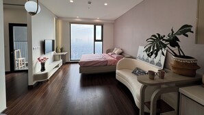 A modern bedroom with a large window, a bed, a sofa, and a dining table.
