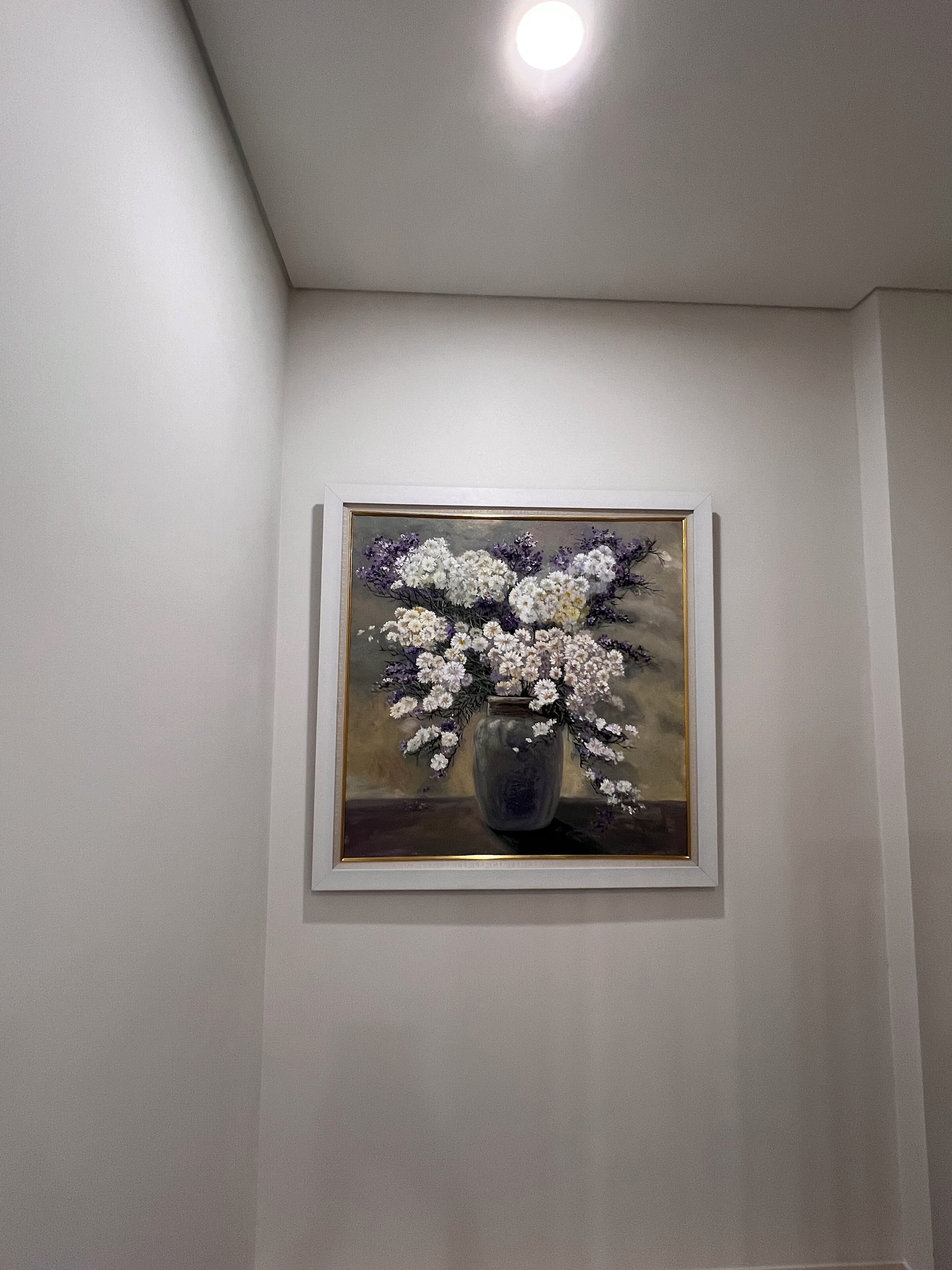 Un cuadro enmarcado con un jarrón y flores sobre una pared.