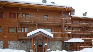 Un immeuble en bois à plusieurs étages, doté d’une base en pierre, de balcons et d’une entrée recouverte de neige.