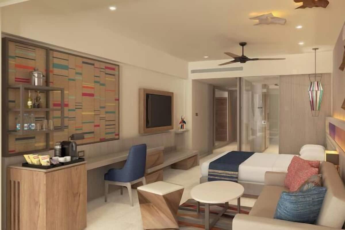 Habitació d'hotel moderna amb zona de seients, televisió, ventilador de sostre i minibar.