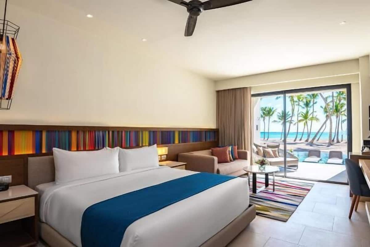 Habitació d'hotel amb un llit gran, una escriptori, una cadira, un sofà, una taula petita i vista a la platja.