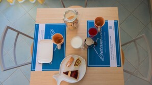 Una mesa de desayuno con un mantel individual azul, un plato blanco con pastelería, un tarro de vidrio, una taza y un vaso de leche.