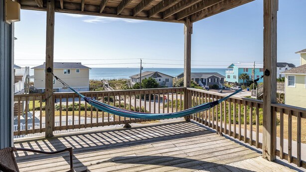 A wooden deck with a hammock, overlooking a residential area and the ocean.