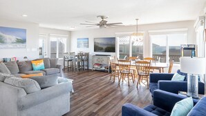 A spacious living room with a gray sofa, blue armchair, and wooden dining table with chairs.