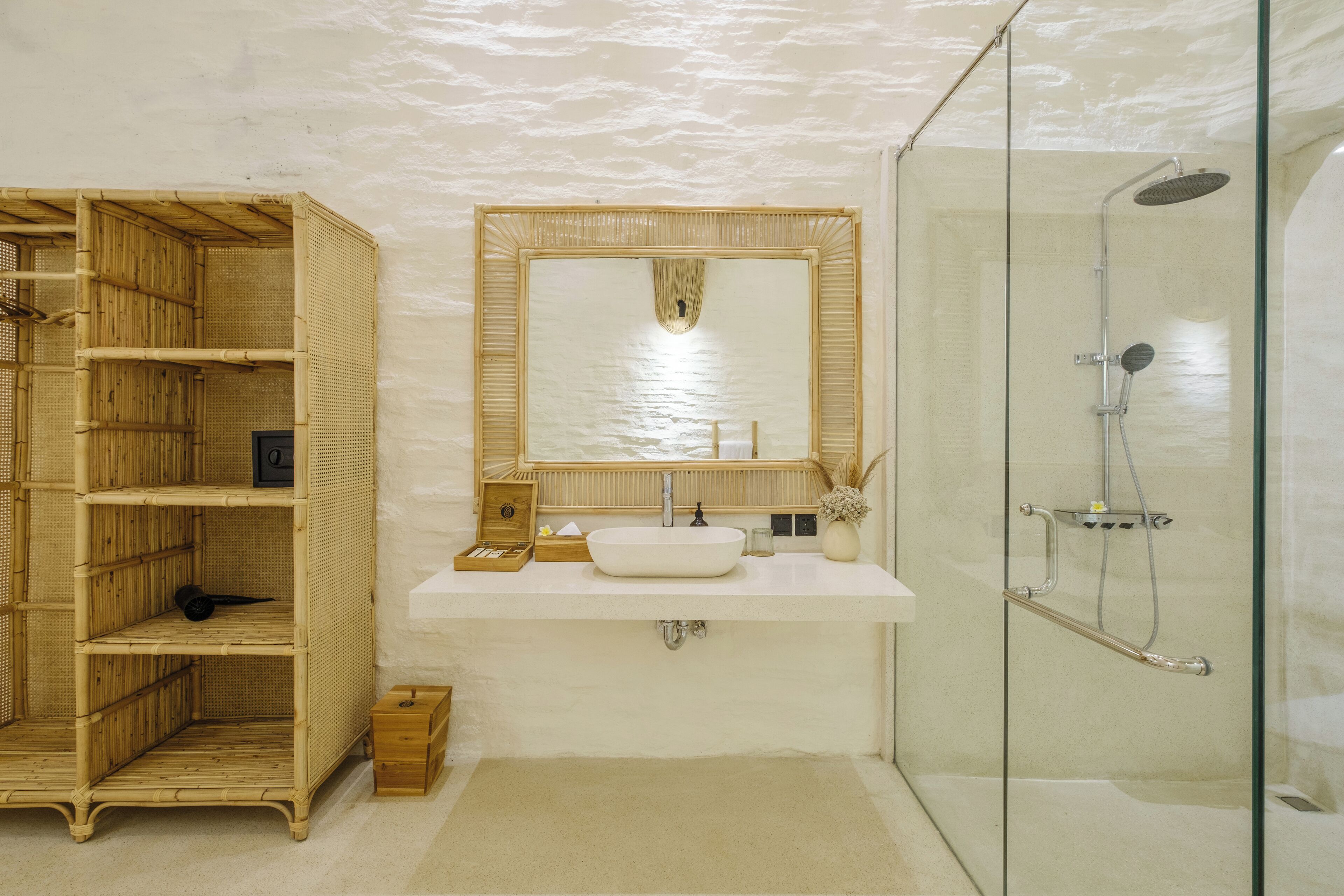 A bathroom with a glass shower enclosure, a white sink with a large mirror, and a bamboo shelf unit.