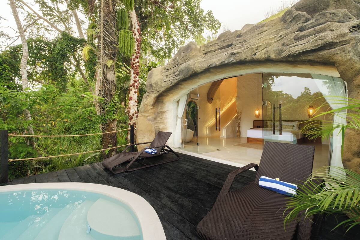 A luxurious outdoor lounge area with a hot tub, reclining chairs, and a glass-enclosed space with a bed.