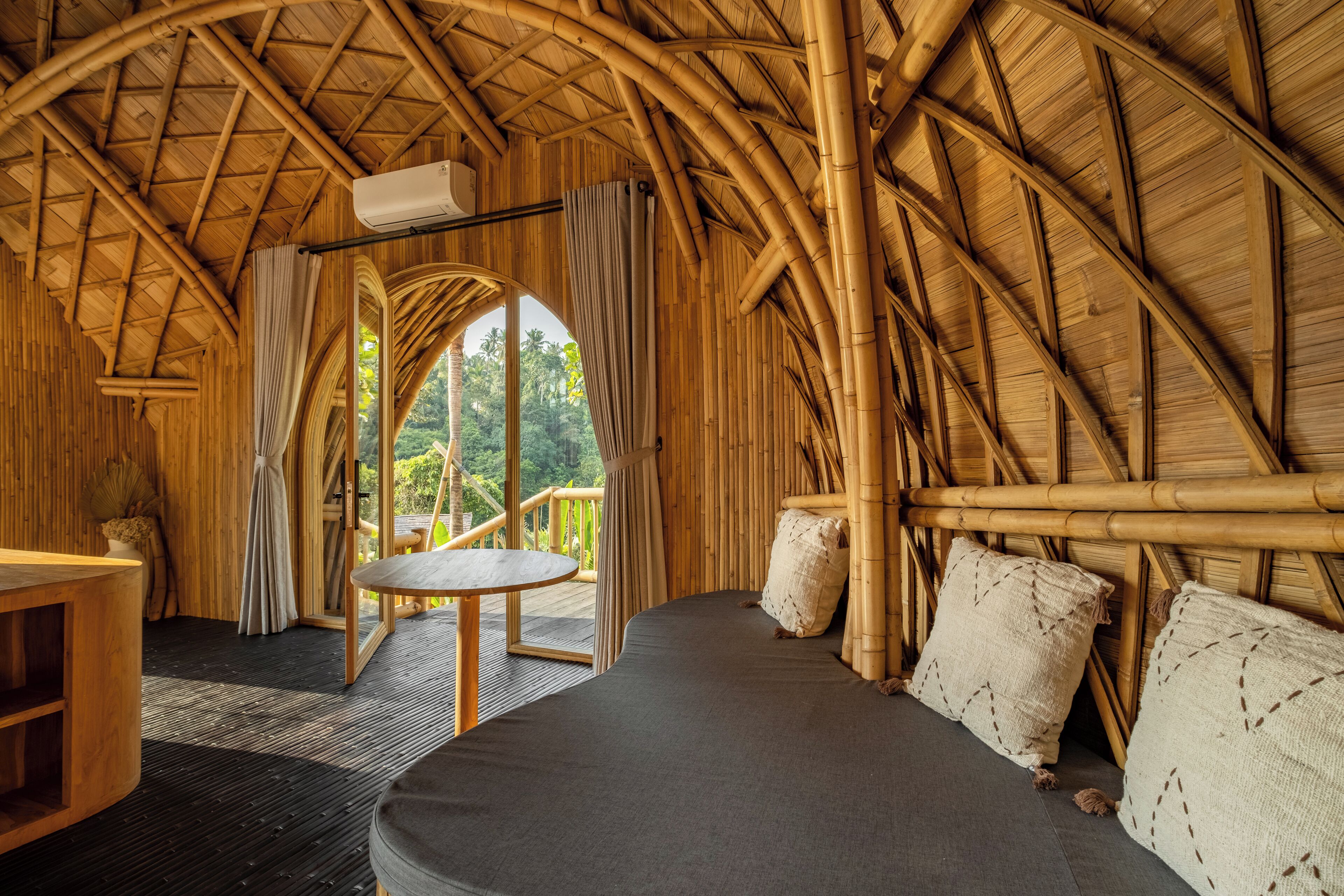 A room with a curved bamboo ceiling, a round table, and a sofa with cushions.