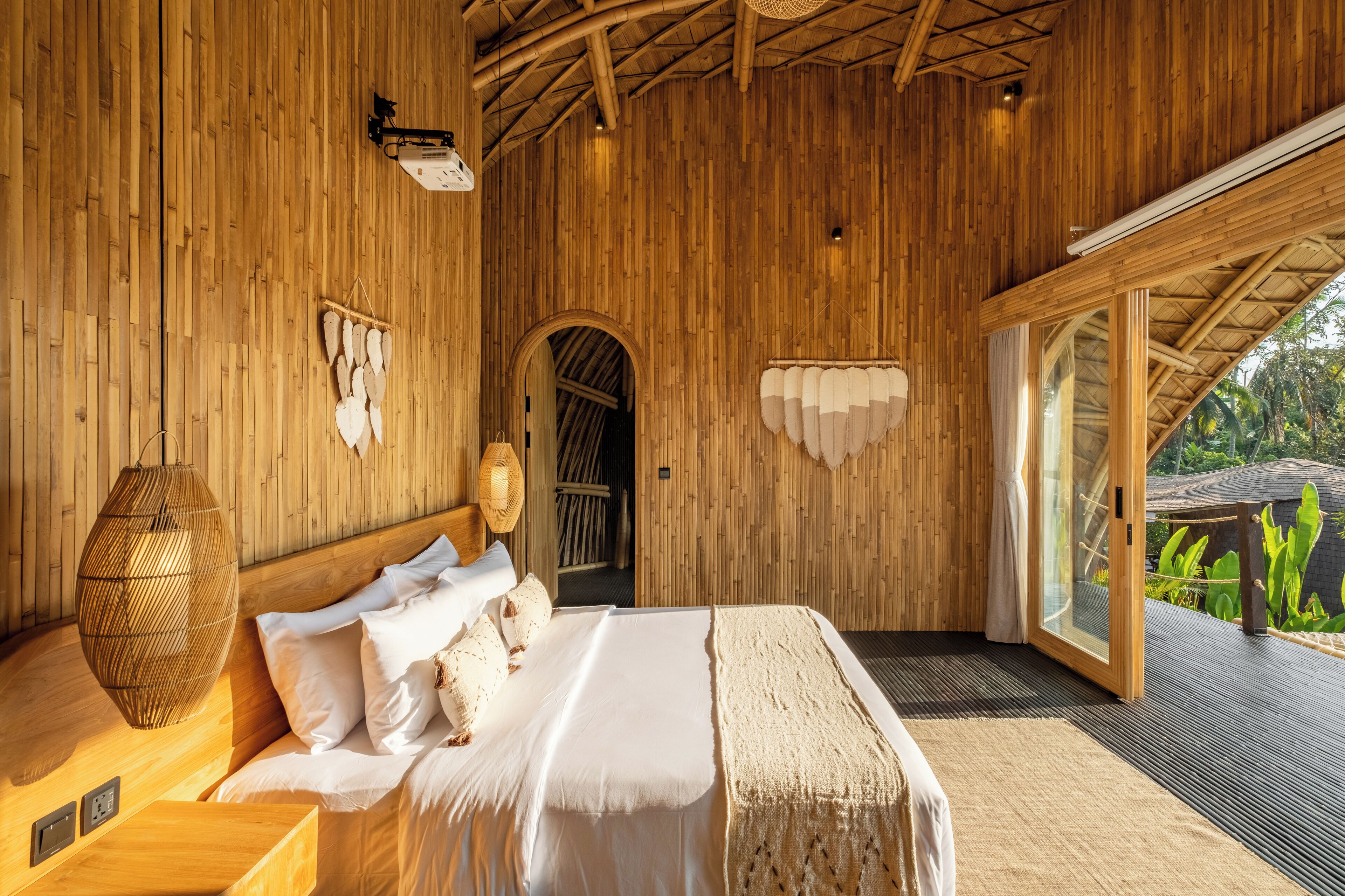 A wooden room with a bed, a hanging light fixture, and a door leading outside.