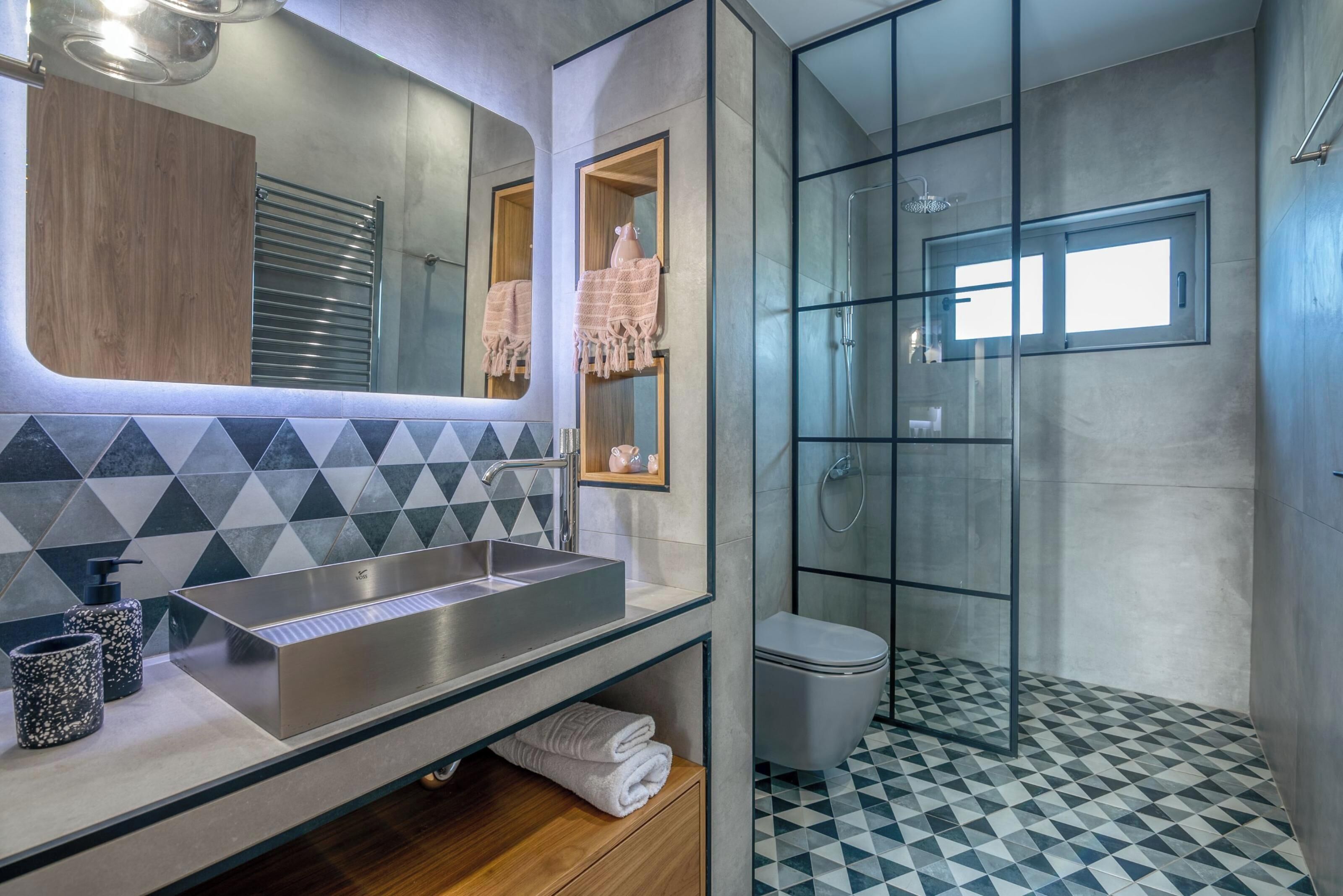 A modern bathroom with a large mirror, a rectangular sink, and a glass-enclosed shower.