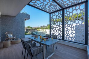 A modern outdoor dining area with a glass table, wicker chairs, and a view of the landscape. - Villa Lona (Platanias)