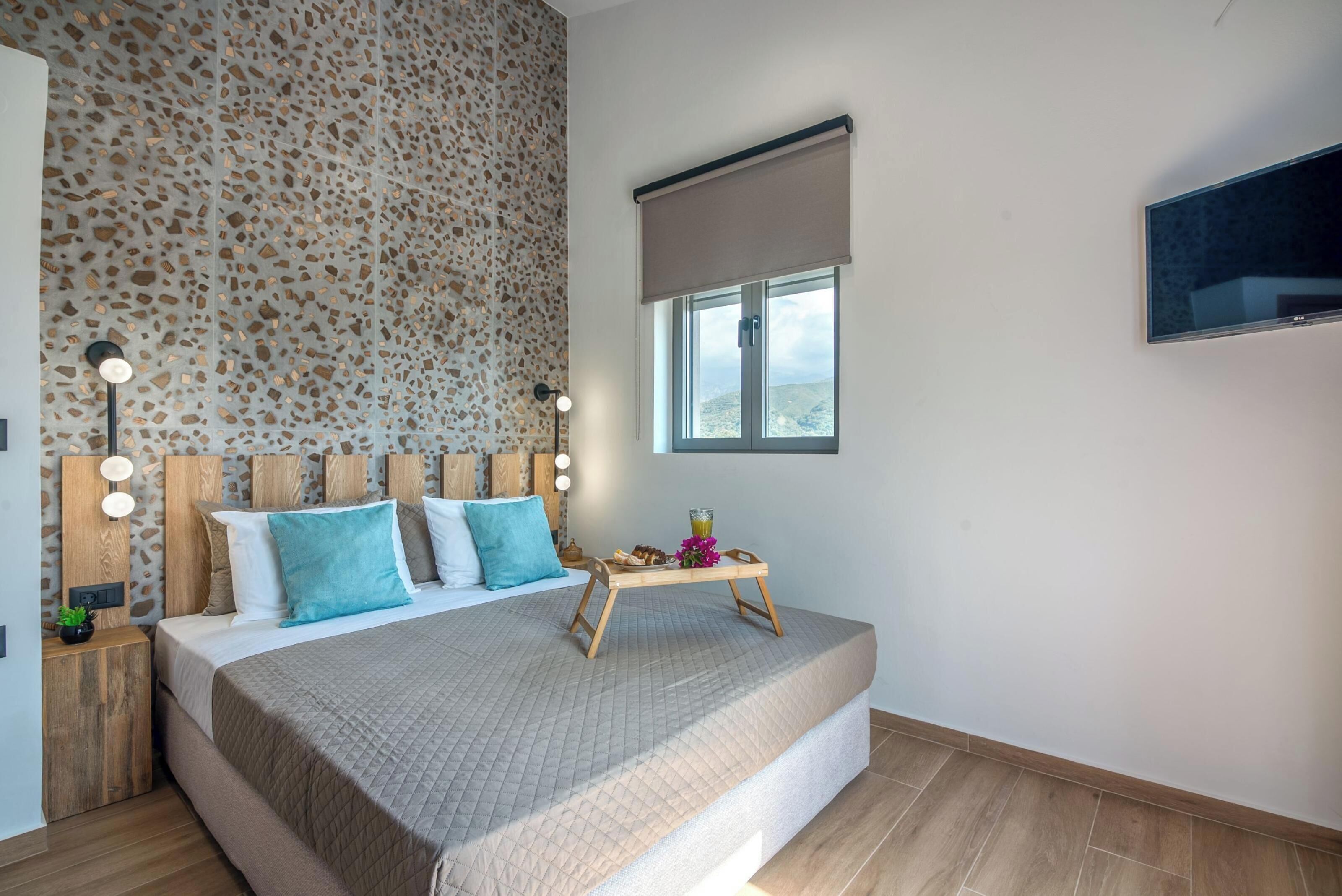A modern bedroom with a large bed, a decorative wall, a bedside table with a lamp, and a window with a view.