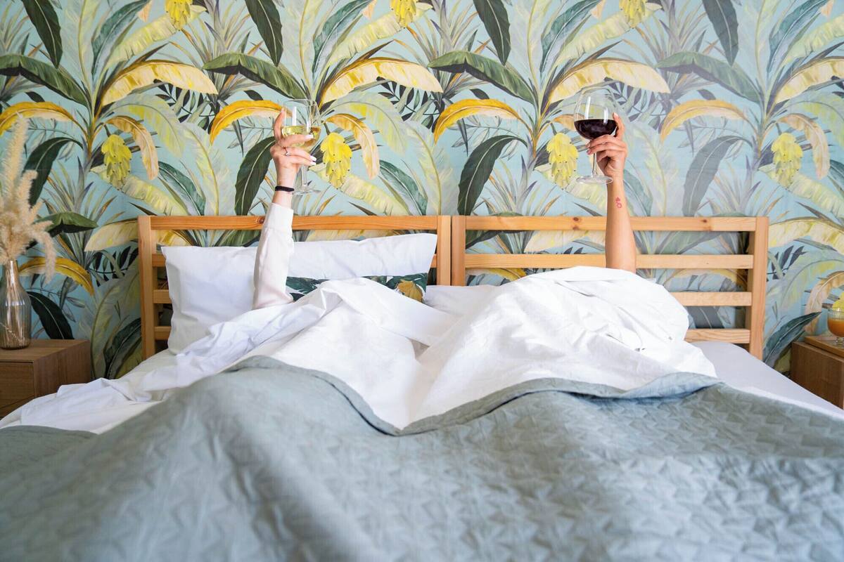 Una cama con cabecera de madera, ropa de cama blanca y un estampado de papel tapiz tropical.