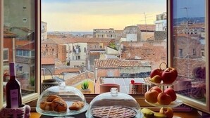 Una mesa con pasteles y una botella, una ventana con vista a la ciudad y un cielo despejado.