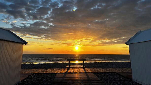 A sunset view from a wooden deck with a bench, overlooking the sea, and two white buildings on either side. - 700m from the sea, apartment with terrace, parking and pétanque court. (Cayeux-sur-Mer)