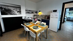 A compact kitchen with a dining area, featuring a tiled floor, a microwave, a refrigerator, and a dining table set with plates and glasses. - 700m from the sea, apartment with terrace, parking and pétanque court. (Cayeux-sur-Mer)