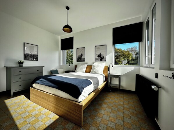 Une chambre moderne avec un lit en bois, une commode et une fenêtre donnant sur un paysage verdoyant.